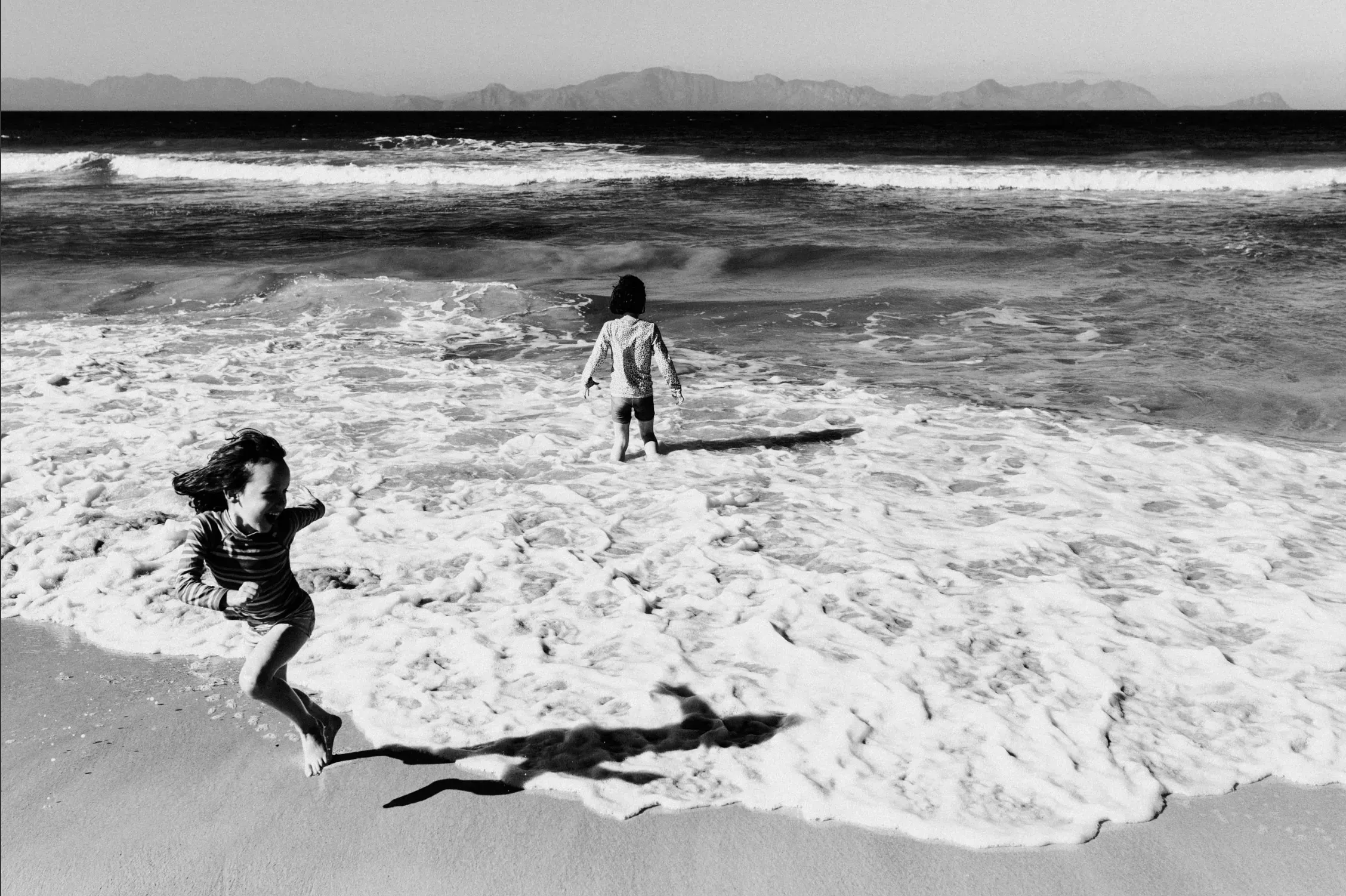 Two children running through the sea on a family day at the beach